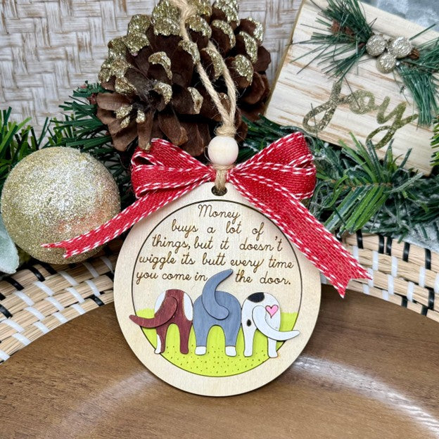 Decorative Christmas ornament with a red bow, pine cone, and cartoon dogs on a wooden surface.