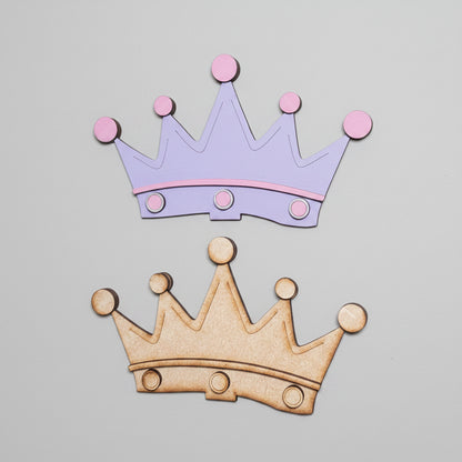 Two MDF crown cutouts with layered pieces, one painted purple with pink accents and one is unpainted