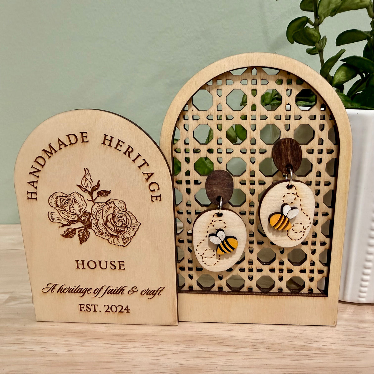 A pair of handmade wood earrings featuring a Busy Bee design. The earrings are crafted from birch wood with a bright yellow bee on a natural wood base with the bee's winding path engraved on it. They have hypoallergenic findings, available in stainless steel studs or clip-ons, or gold-plated clip-ons. The earrings are approximately 1 inch wide by 2 inches tall, with a satin finish and a total thickness of 0.5 inches. Perfect for nature-themed events and eco-friendly fashion.