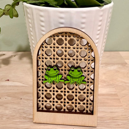 A pair of handmade wooden earrings featuring a smiling frog design, crafted from birch wood with a gloss finish. Available in bright and vintage green colors, these earrings offer hypoallergenic stainless steel and gold-plated options. The earrings are approximately 1 inch wide and 0.75 inches tall, suitable for nature lovers and those seeking unique, personalized jewelry pieces. Custom color options are available upon request, making these earrings a versatile accessory for various occasions.