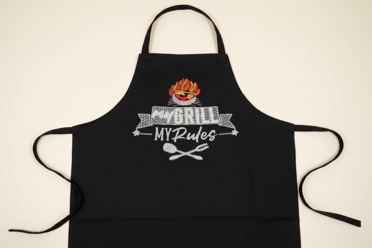 Black apron with embroidered design of a grill, text 'my GRILL MY Rules', and grill utensils