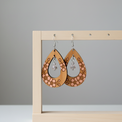Wooden earrings with floral patterns hanging on a wooden stand against a gray background