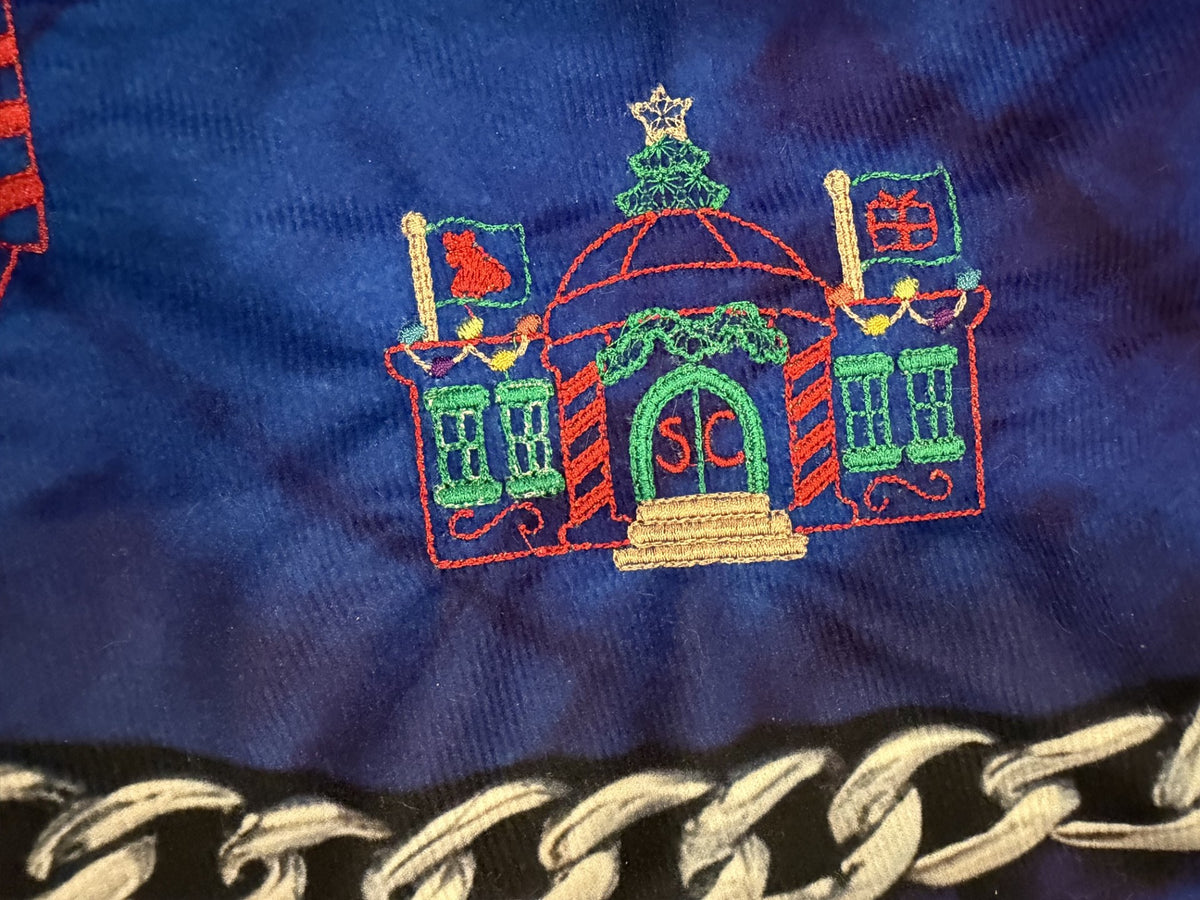 Northpole Village tree skirt with a sketch style embroidery on a blue background.