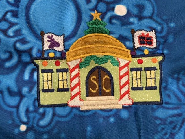 Northpole Village tree skirt with applique embroidery on a blue background.