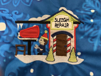 Northpole Village tree skirt with applique embroidery on a blue background.