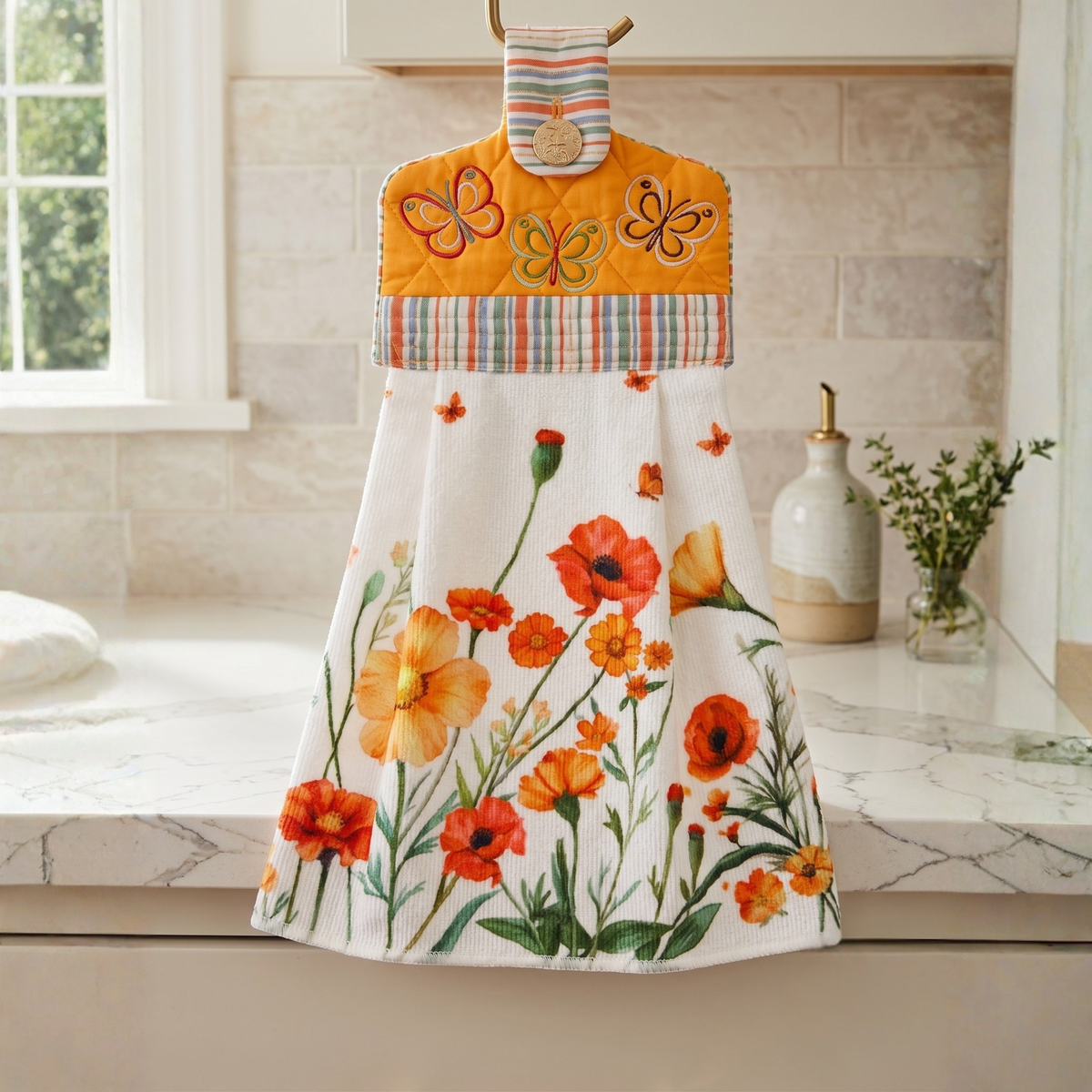 A hanging kitchen towel featuring a watercolor style print of red and orange flowers and butterflies. The top section is orange with a quilted texture, embroidered butterflies, a striped patterned fabric border, with a button closure.