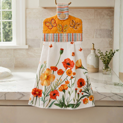 A hanging kitchen towel featuring a watercolor style print of red and orange flowers and butterflies. The top section is orange with a quilted texture, embroidered butterflies, a striped patterned fabric border, with a button closure.