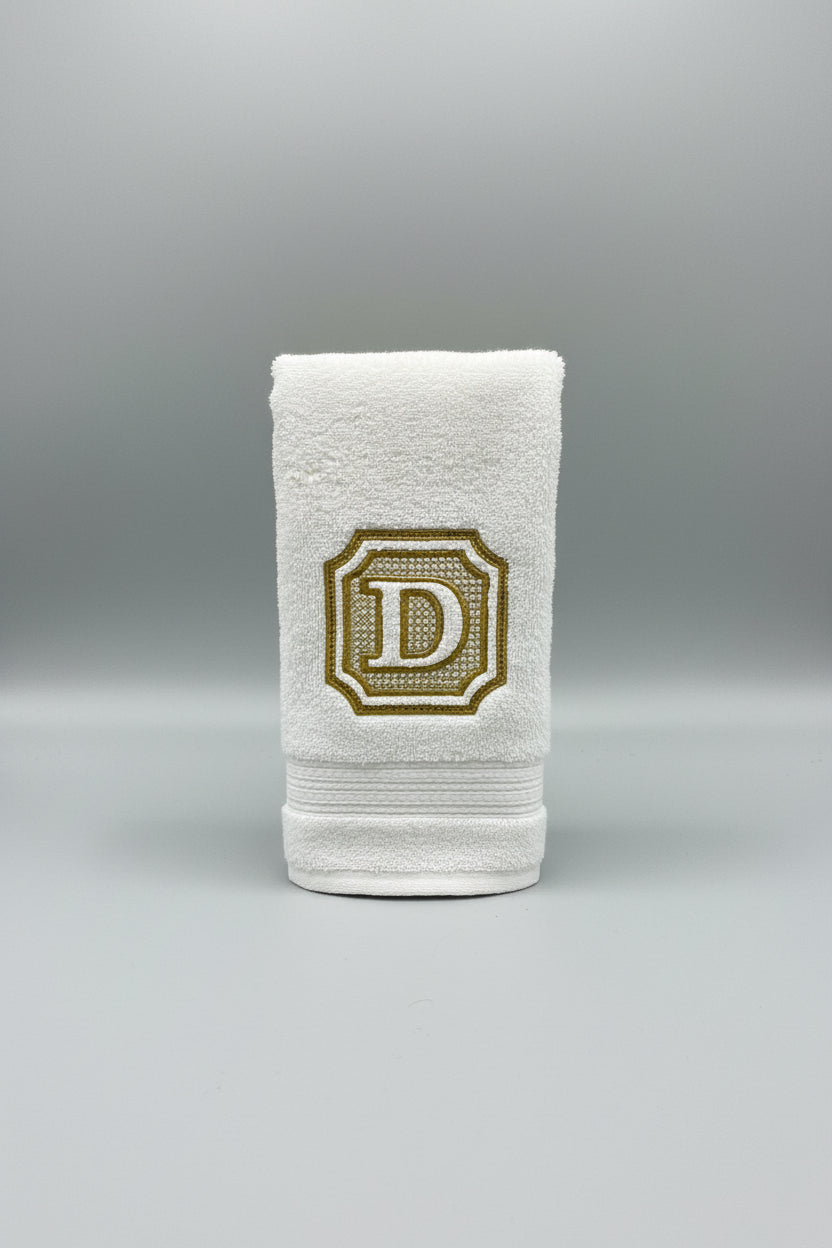 White towel with a gold embroidered letter 'D' on a gray background