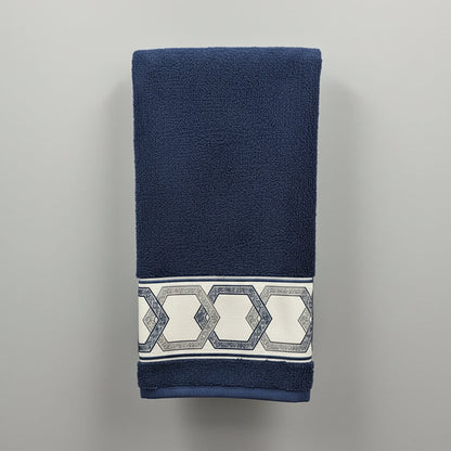 Blue towel with decorative pattern hanging on a black rack against a white tiled wall.