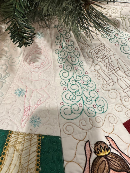 Detail view of a handcrafted white Christmas tree skirt featuring detailed embroidered Nutcracker Ballet characters around the border with detailed quilting in the center. Close up of quilting.