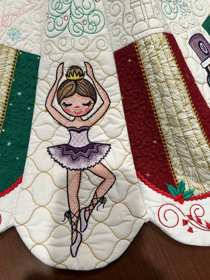 Detail view of a handcrafted white Christmas tree skirt featuring detailed embroidered Nutcracker Ballet characters around the border with detailed quilting in the center. Close up of Sugar Plum Fairy.