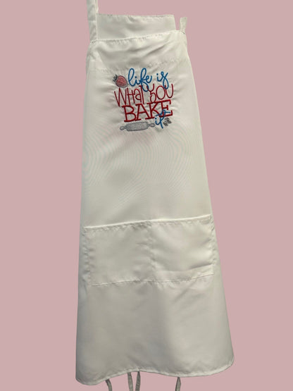 White apron with 'Life is what you bake' text on a pink background